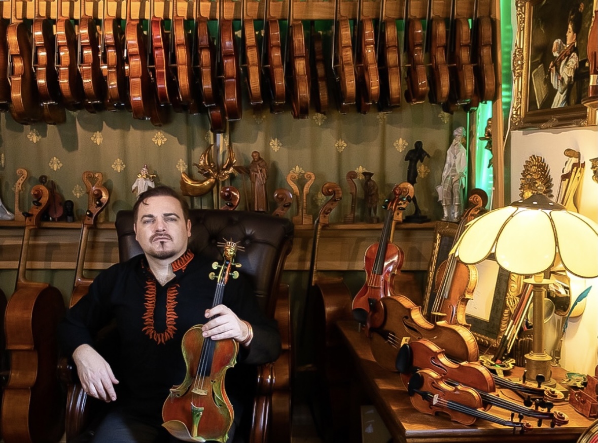 Pictured is Lukas Wronski in his shop, with violins and artwork lining the walls. (Photo used by permission of Lukas Wronski)