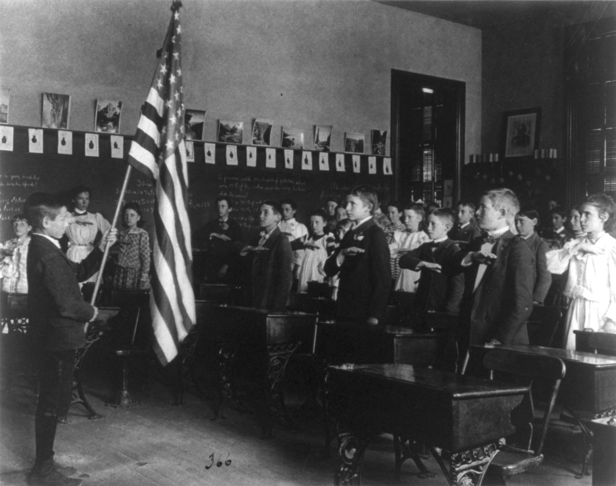 Students in a Washington, D.C. classroom recite the Pledge of Allegiance in 1899, reflecting the historical role of public schools in shaping national identity. (Photo Credit: Frances Benjamin Johnston (1864-1952) photographer, Public domain, via Wikimedia Commons)
